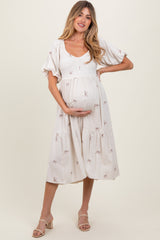woman wearing a cream maternity dress with embroidered bows and a flowing skirt, gently holding her baby bump