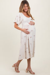 woman wearing a light beige maternity dress with short puff sleeves and bow print, cradling her baby bump
