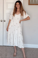 woman wearing a white midi dress with embroidered bow details and puff sleeves, standing in a stylish pose
