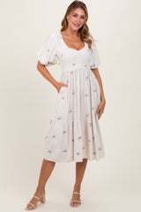 woman wearing a white midi dress with puff sleeves and bow embroidery, standing with hands in pockets
