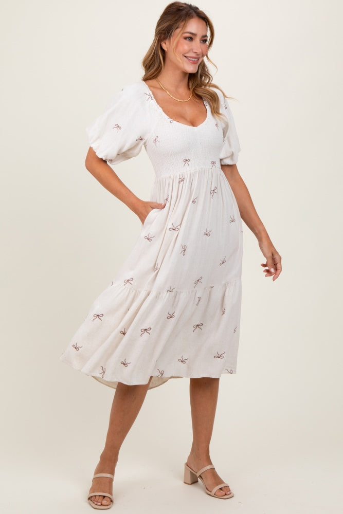 woman wearing a cream midi dress with puff sleeves and bow pattern, featuring a smocked bodice and side pockets