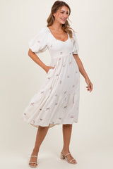 woman wearing a cream midi dress with puff sleeves and bow pattern, featuring a smocked bodice and side pockets