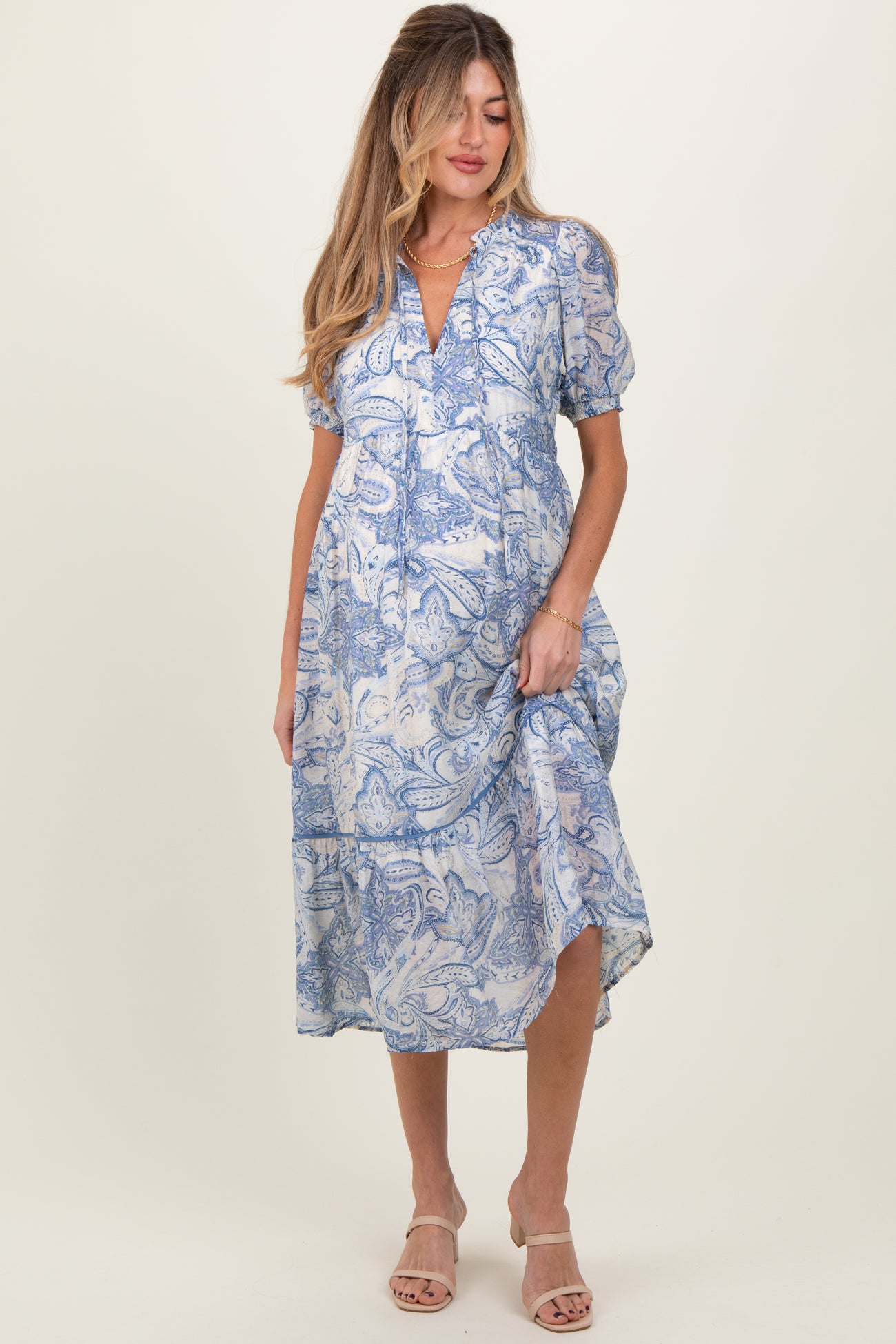woman wearing a blue and white paisley print maternity dress with short sleeves and a tiered hem, showing her baby bump