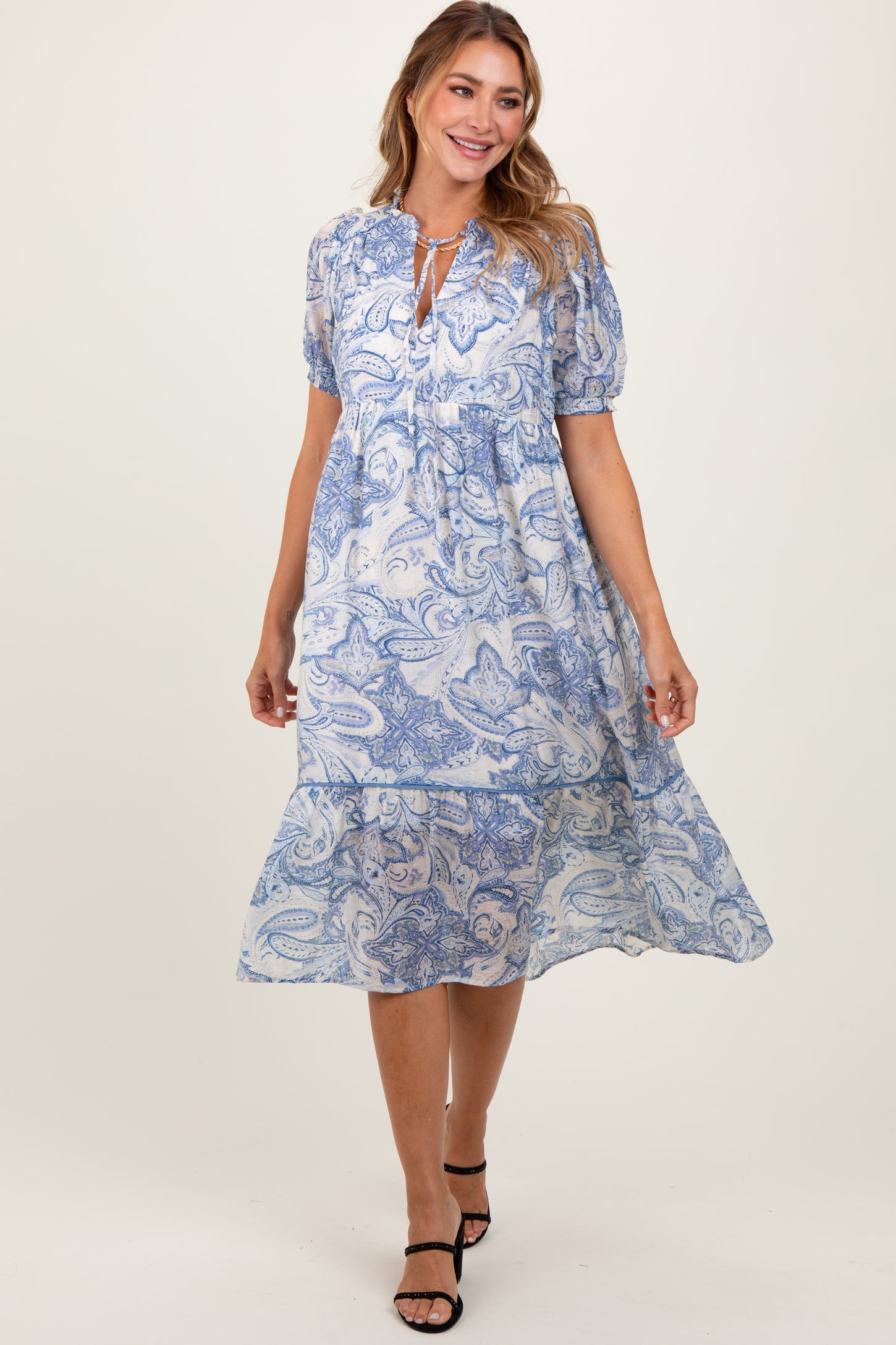 woman wearing a blue and white paisley print midi dress with puff sleeves and a tie neckline