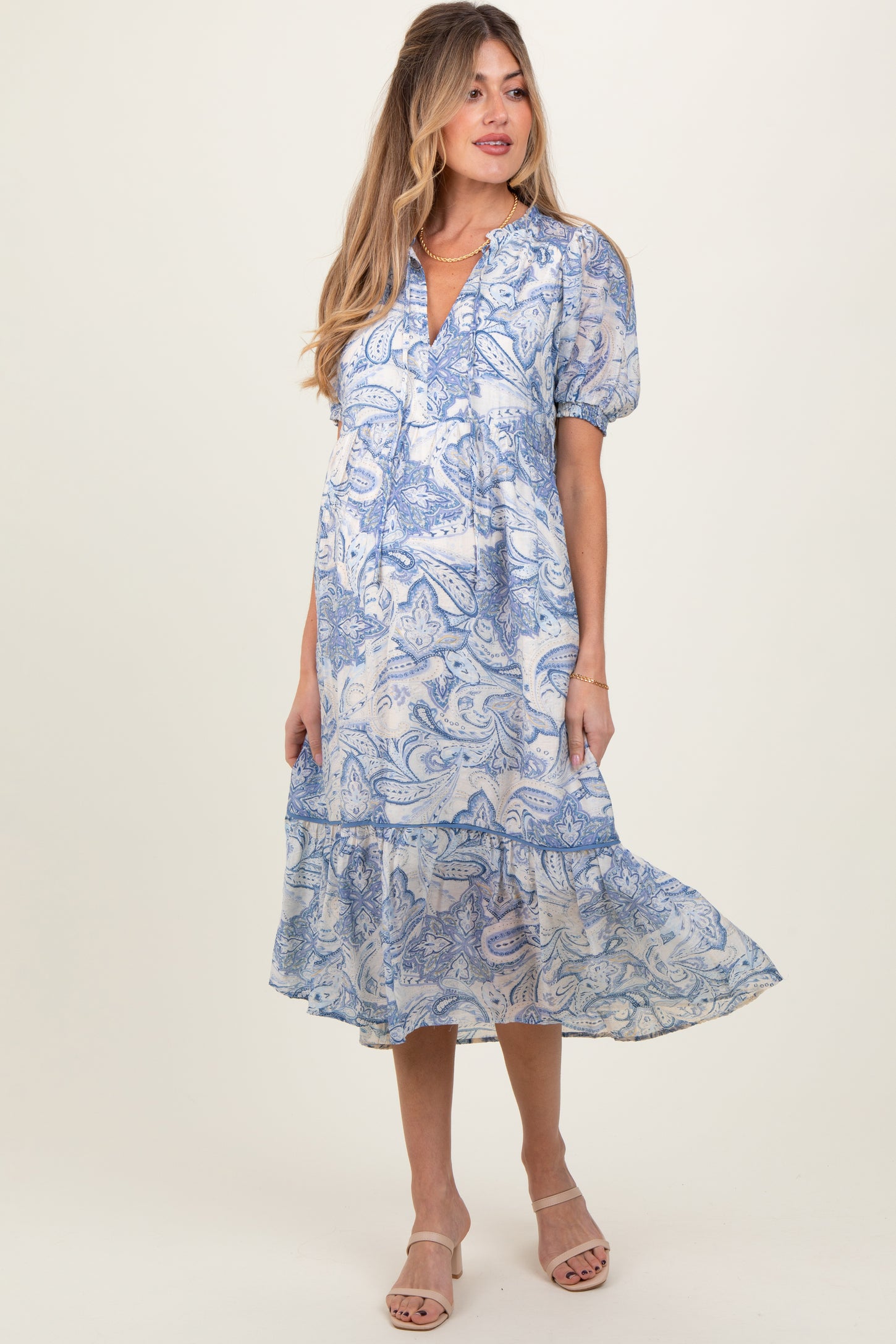 woman wearing a blue paisley print maternity dress with puff sleeves and a tiered hemline, showcasing her baby bump