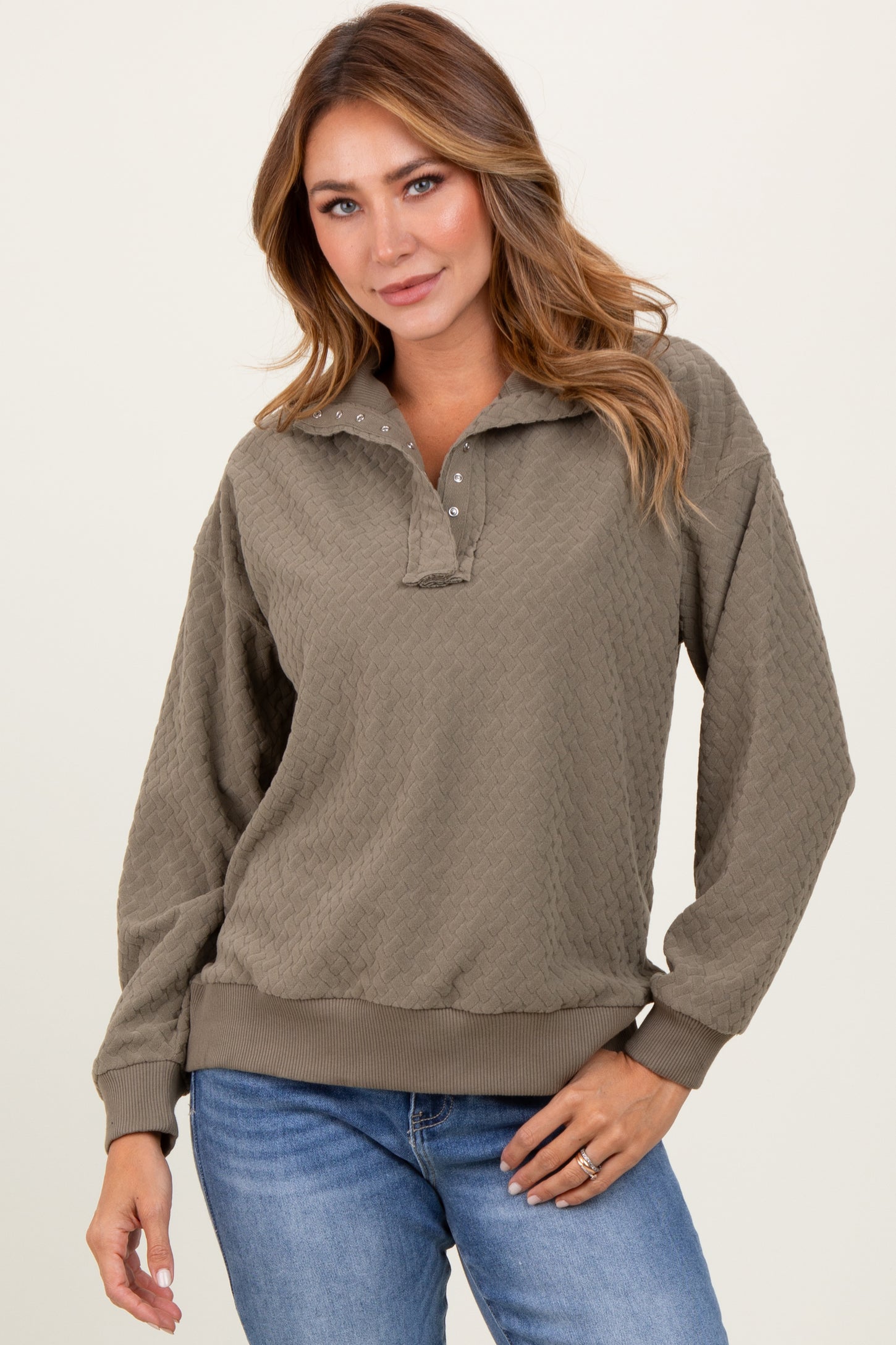 woman wearing a olive green textured pullover with a collar and button details, paired with blue jeans