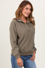 woman wearing a taupe pullover sweatshirt with a half zip and textured pattern, paired with blue jeans.