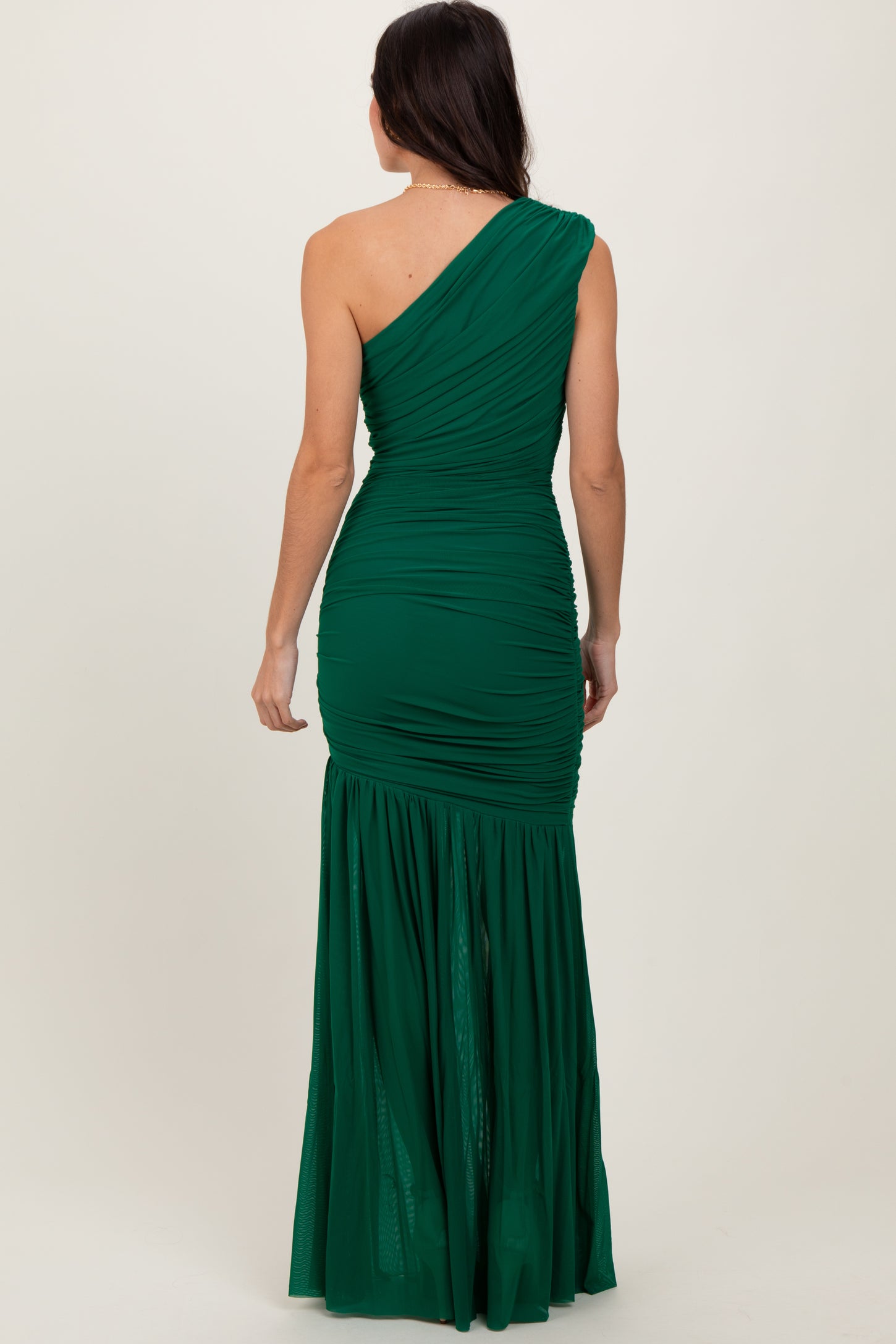 woman wearing a green one-shoulder ruched gown with a flowing bottom, view of the back