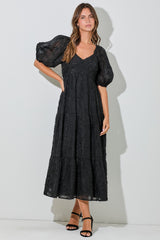 woman wearing a black tiered midi dress with puff sleeves and a v-neckline, styled with black strappy heels