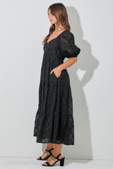woman wearing a black tiered maxi dress with puff sleeves and pockets, styled with black block-heeled sandals