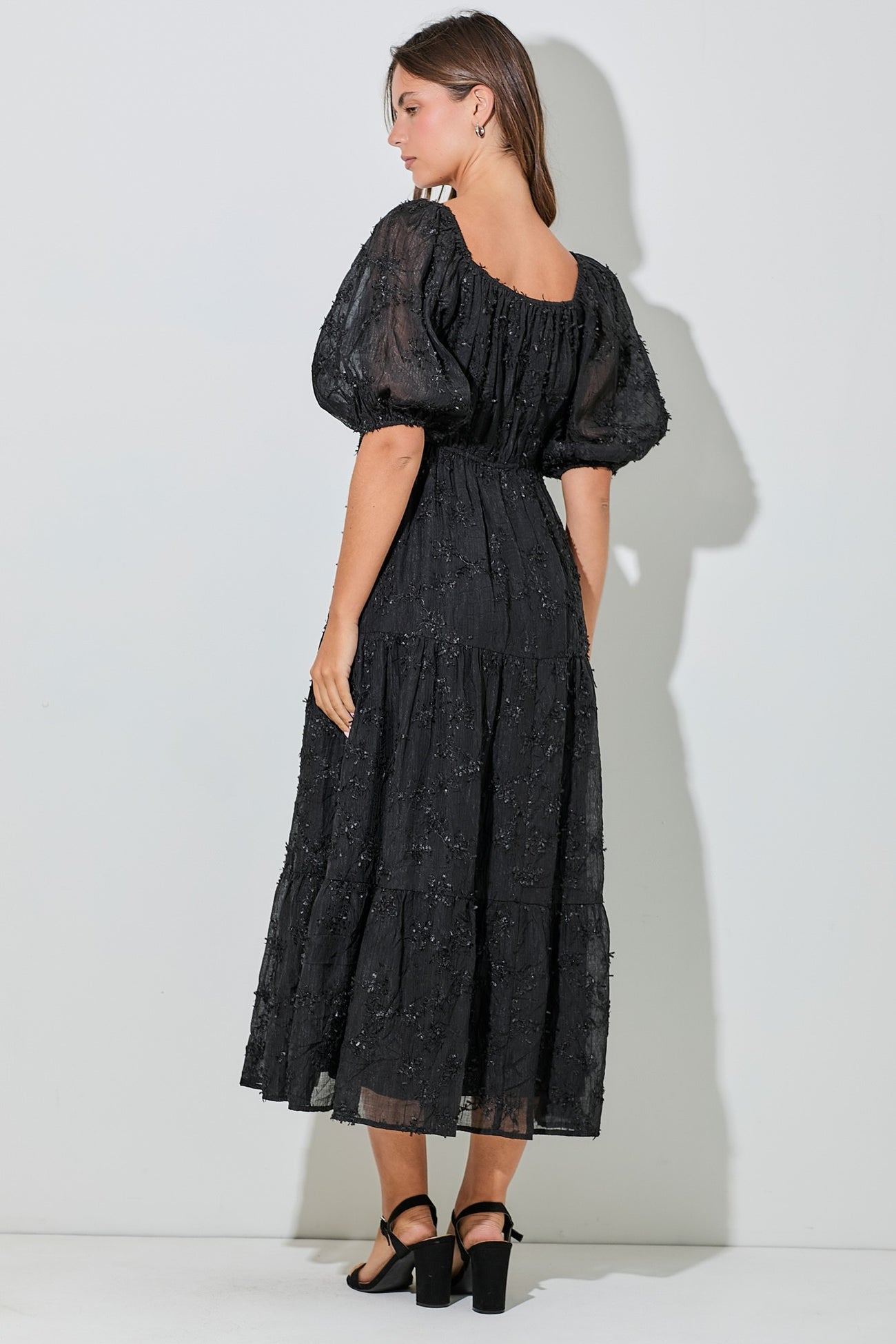 woman wearing a black tiered midi dress with puff sleeves and embellished detailing, shown from the back