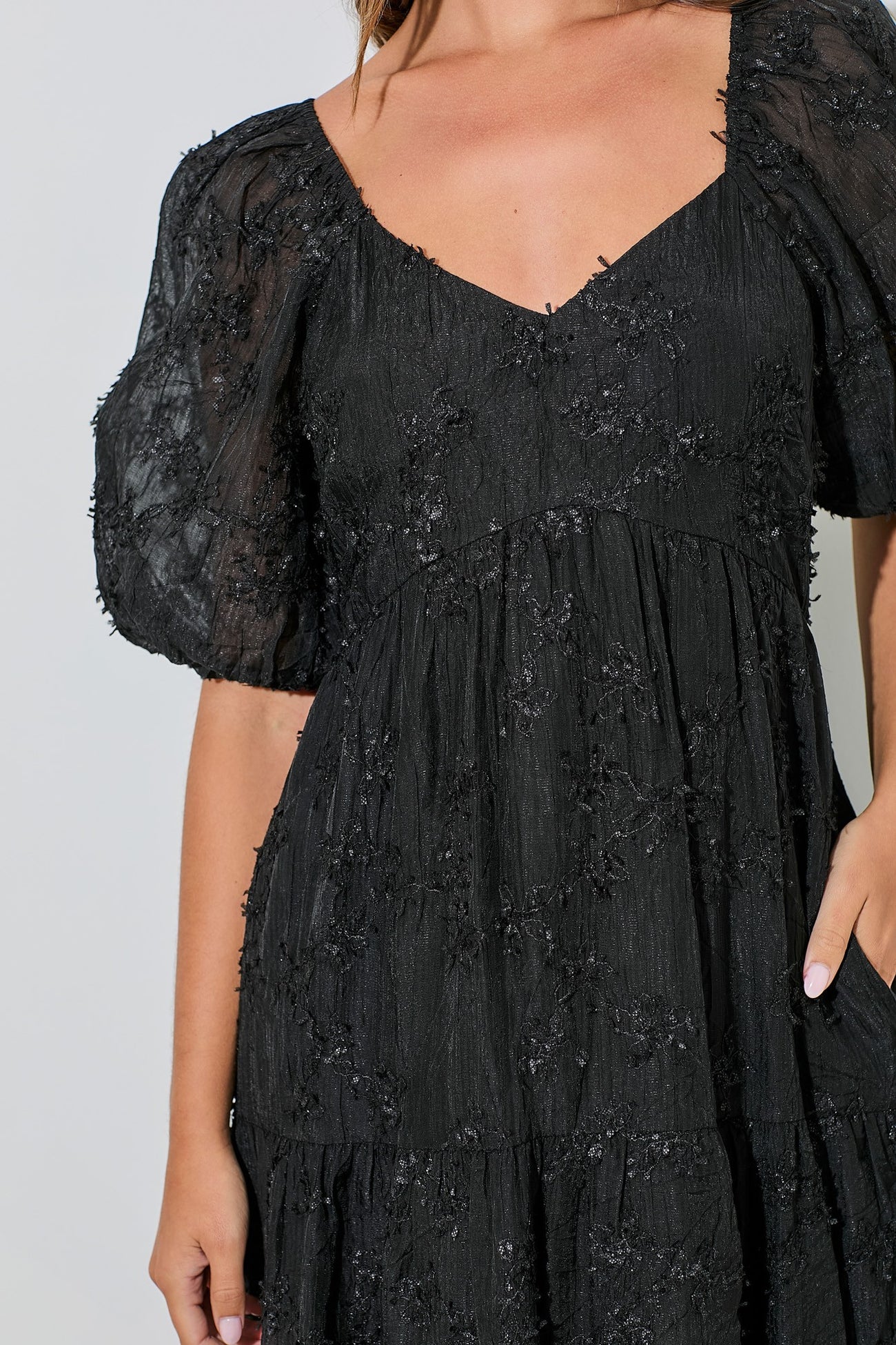 woman wearing a black puff sleeve dress with floral appliqué details and a tiered skirt