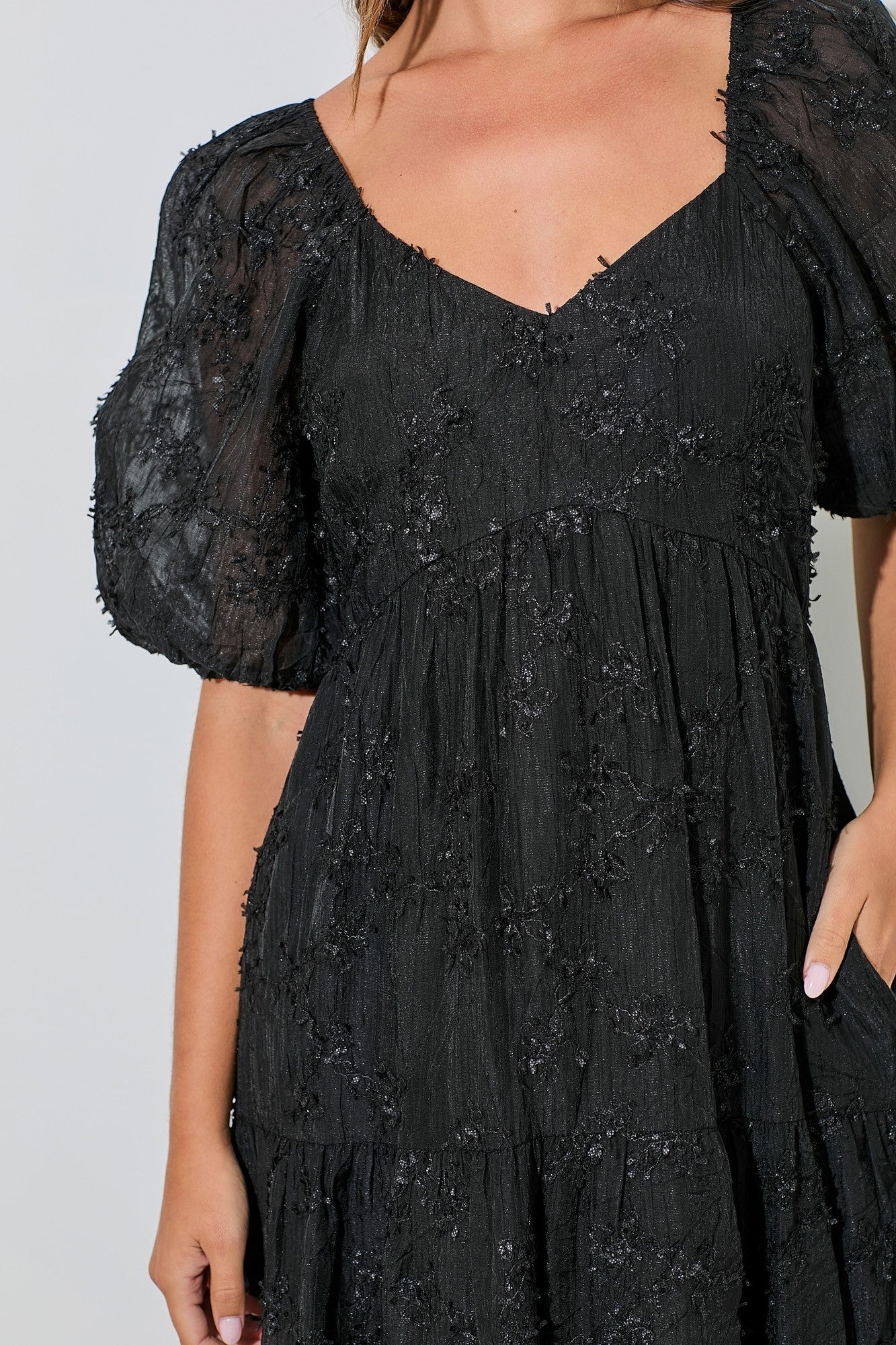 woman wearing a black puff sleeve dress with floral appliqué details and a tiered skirt