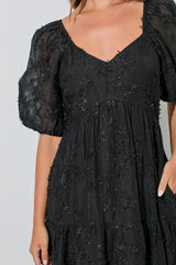 woman wearing a black puff sleeve dress with floral appliqué details and a tiered skirt