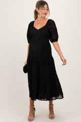 woman wearing a black puff sleeve maternity dress with a tiered design and visible baby bump