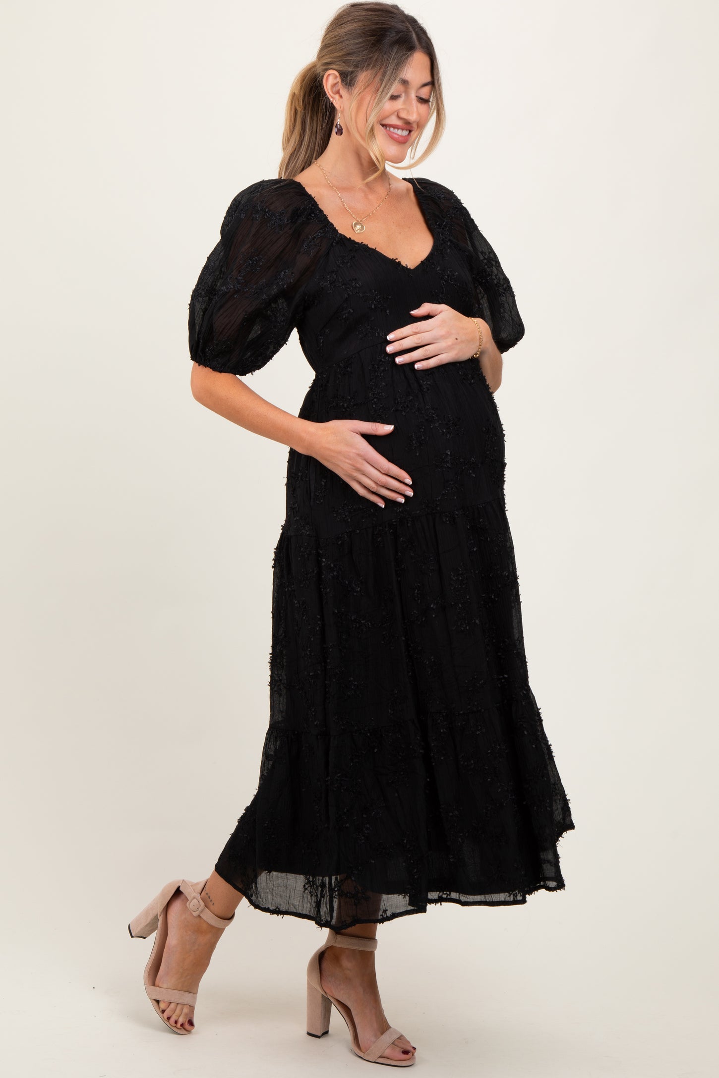 woman wearing a black puff sleeve maternity dress with a tiered skirt and holding her baby bump