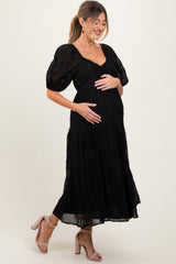 woman wearing a black puff sleeve maternity dress with a tiered skirt and holding her baby bump