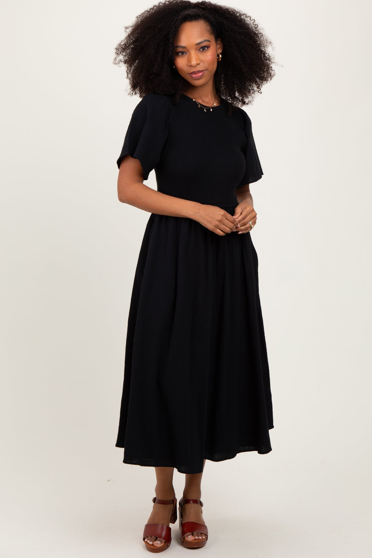 woman wearing a black midi dress with puff sleeves and a fitted bodice, styled with red heeled sandals