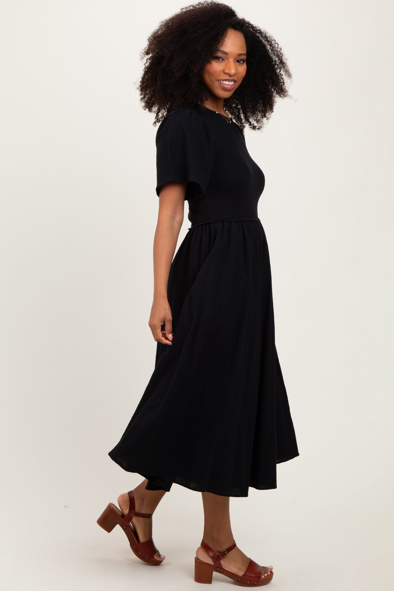 woman wearing a black short sleeve midi dress with a fitted bodice and flowy skirt, smiling to the side