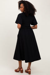 woman wearing a black midi dress with short sleeves and a smocked waist, standing with her back to the camera