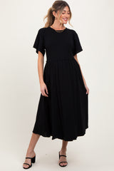 woman wearing a black maternity tiered midi dress with short puff sleeves and a fitted bodice, smiling while posing