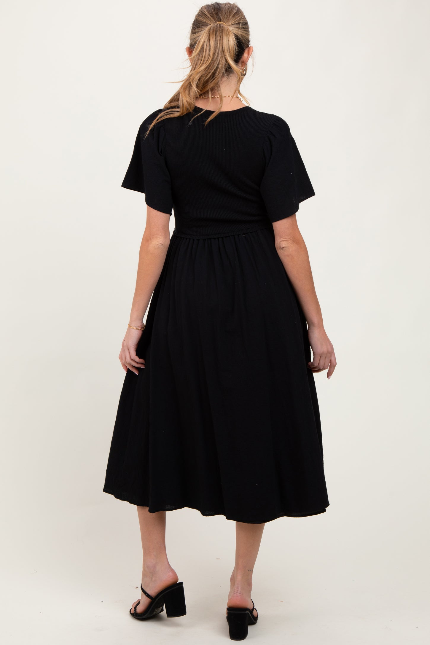 woman wearing a black maternity dress with short sleeves and a flowy skirt, showing a side view of the back design