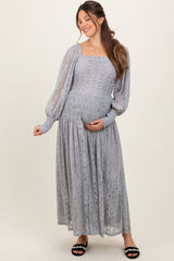 woman wearing a light gray lace maternity dress with long sleeves and a square neckline, holding her baby bump