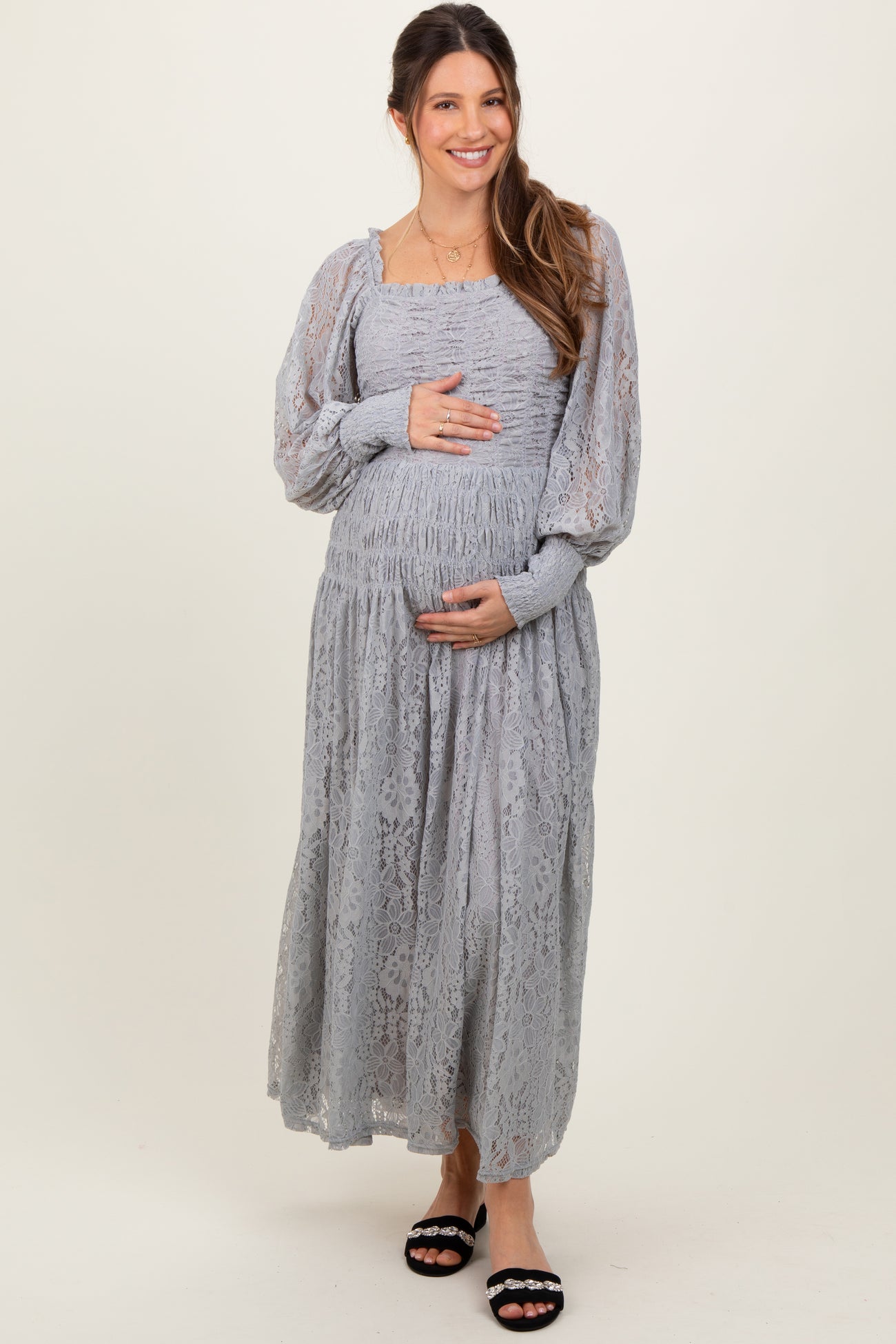 woman wearing a gray lace maternity dress, smiling and touching her baby bump
