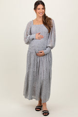 woman wearing a gray lace maternity dress, smiling and touching her baby bump