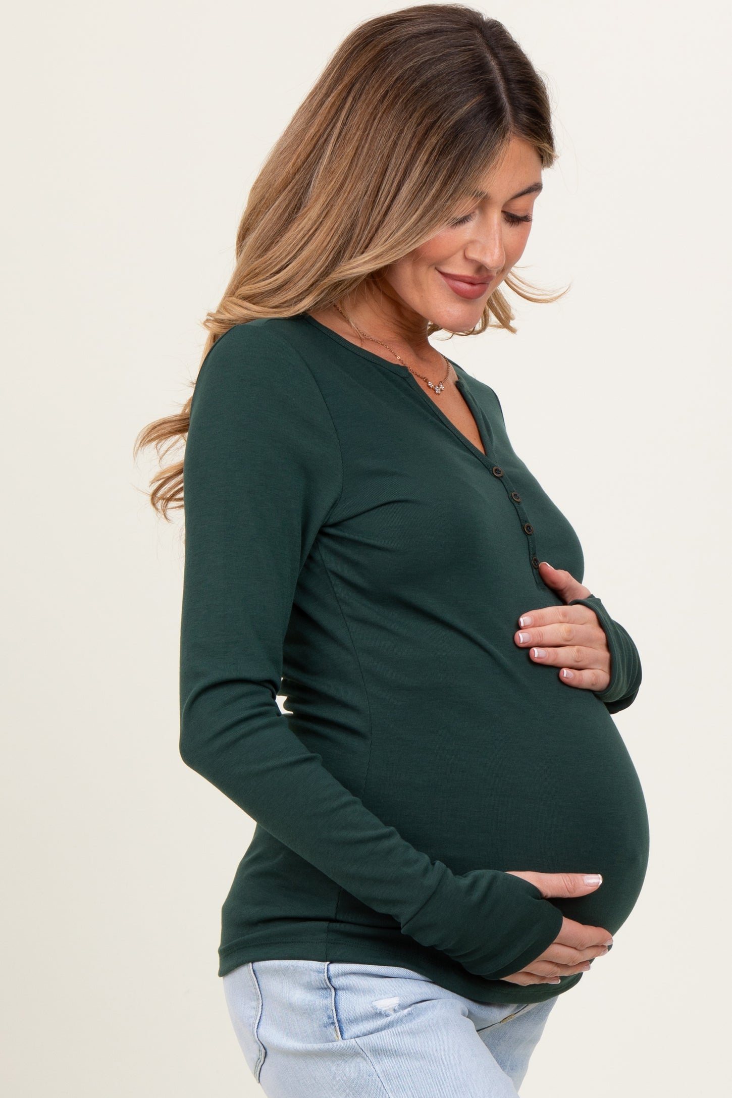 woman wearing a dark green long sleeve maternity top and holding her baby bump
