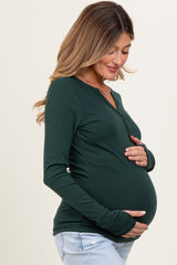 woman wearing a dark green long sleeve maternity top and holding her baby bump