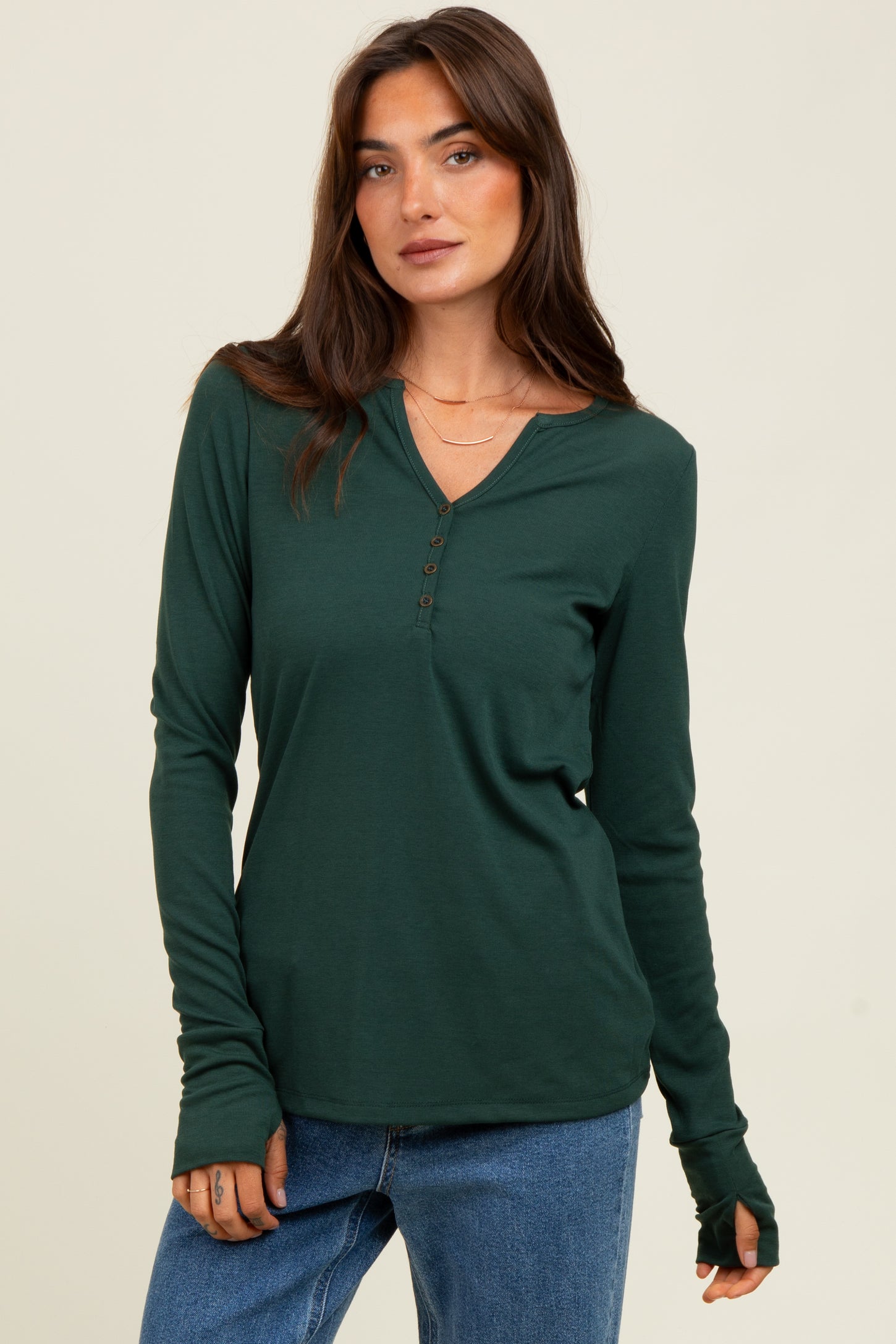 woman wearing a dark green long sleeve henley top with buttons and thumbhole cuffs, paired with blue jeans