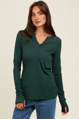 woman wearing a dark green long sleeve henley top with buttons and thumbhole cuffs, paired with blue jeans