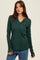 woman wearing a dark green long sleeve henley top with buttons and thumbhole cuffs, paired with blue jeans