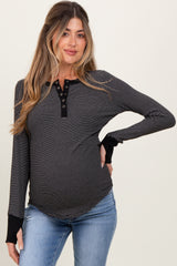 woman wearing a black and white striped maternity top with buttons and long sleeves, showcasing her baby bump