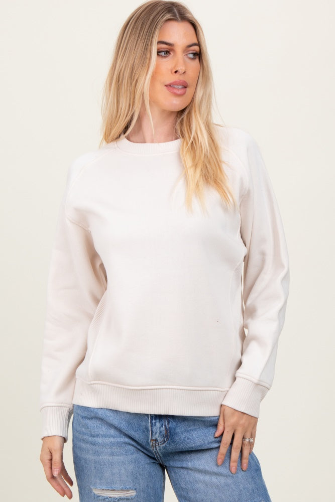 woman wearing a cream long sleeve sweatshirt with ribbed cuffs and a relaxed fit, paired with blue jeans