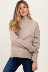 woman wearing a beige maternity sweater with a high neck and relaxed fit, styled with blue jeans