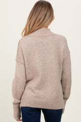 woman wearing a beige oversized maternity sweater with a high neckline and relaxed fit, seen from the back