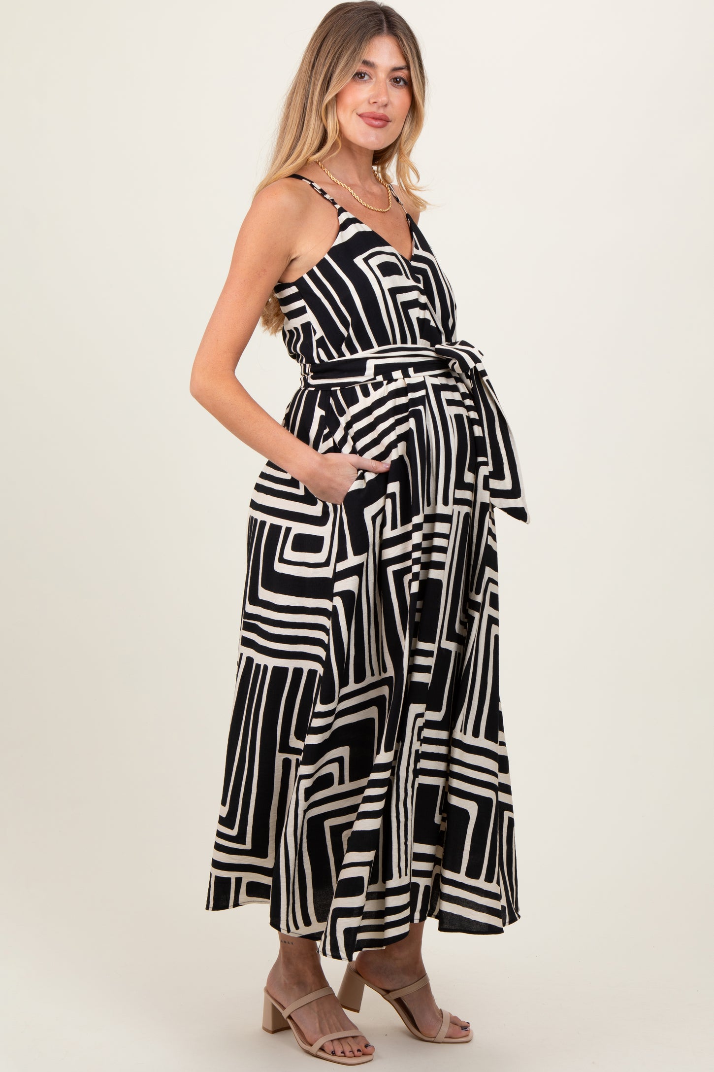 woman wearing a black and white geometric print maternity maxi dress with a tie waist and pockets, showcasing her baby bump