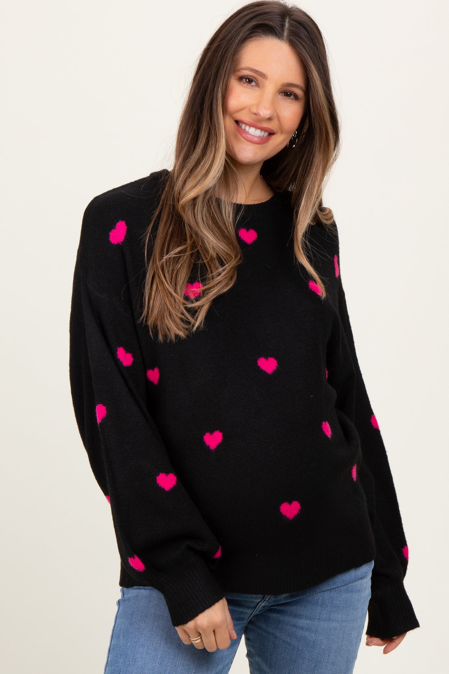 woman wearing a black maternity sweater with pink heart patterns and a visible baby bump