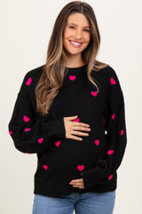 woman wearing a black maternity sweater with pink heart patterns and holding her baby bump