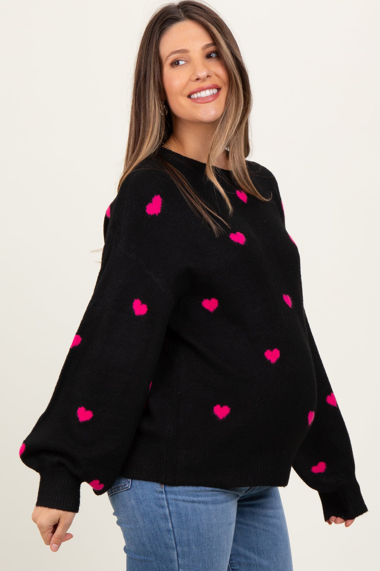 woman wearing a black maternity sweater with pink heart patterns and a visible baby bump