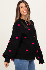 woman wearing a black maternity sweater with pink heart patterns and a visible baby bump
