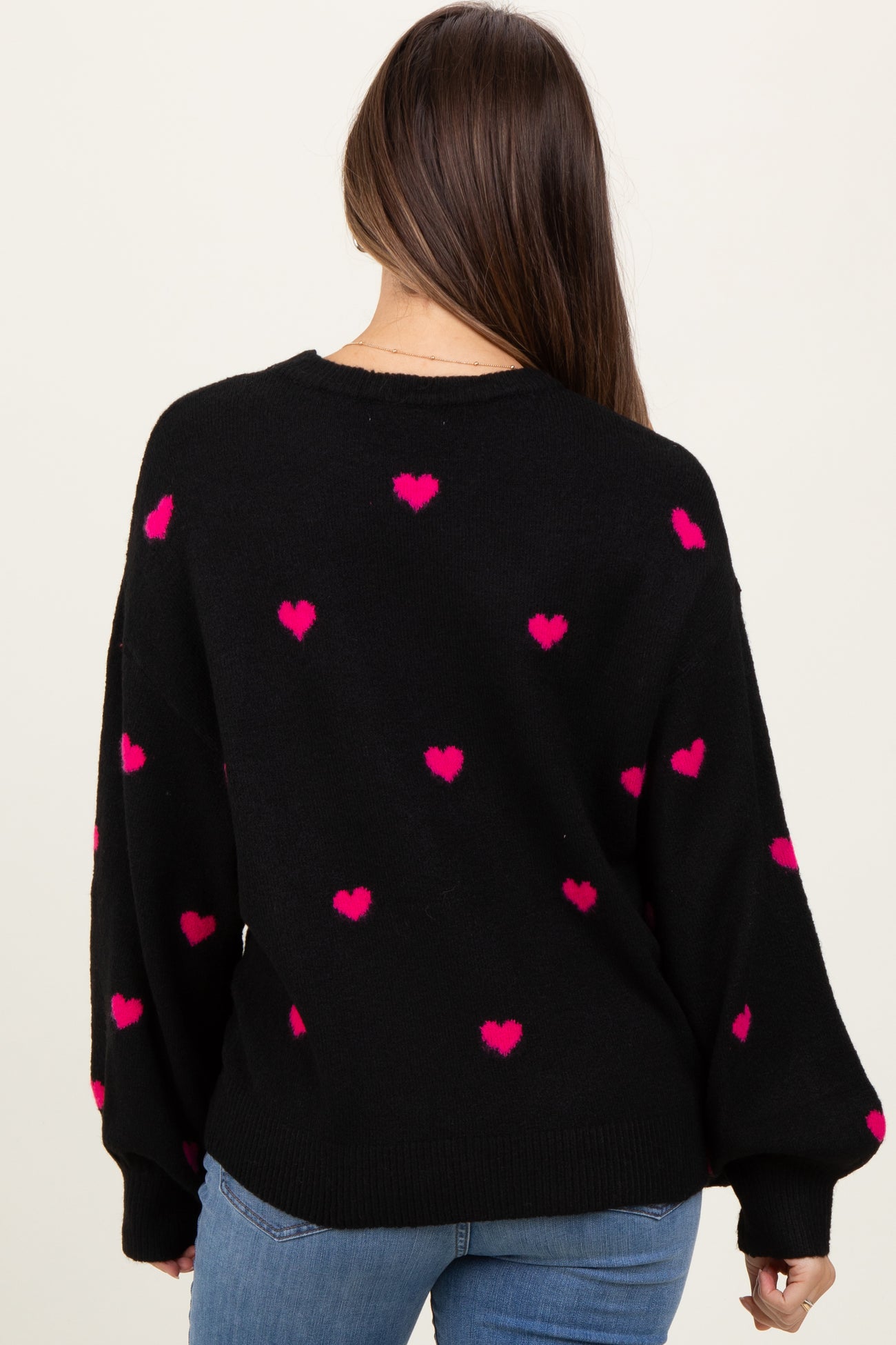 woman wearing a black oversized maternity sweater with pink heart patterns, shown from the back