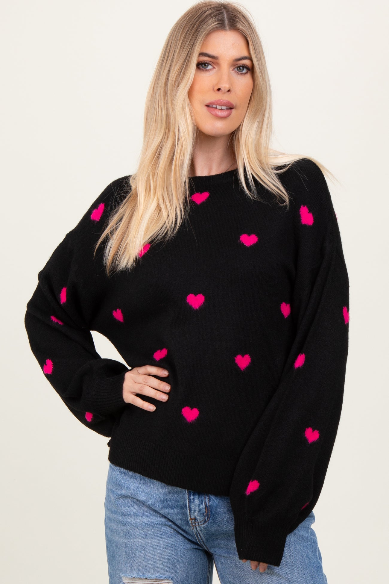 woman wearing a black sweater with pink heart patterns and relaxed fit, paired with light blue jeans