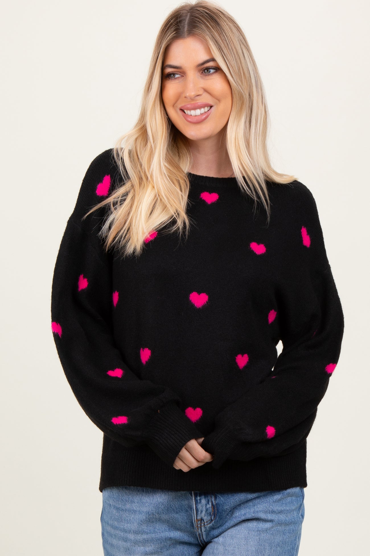 woman wearing a black sweater with pink heart patterns and a relaxed fit, smiling at the camera