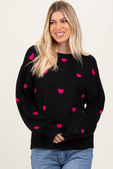 woman wearing a black sweater with pink heart patterns and a relaxed fit, smiling at the camera