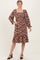 woman wearing a floral pink midi dress with smocked bodice and long sleeves, standing with one hand on her hip