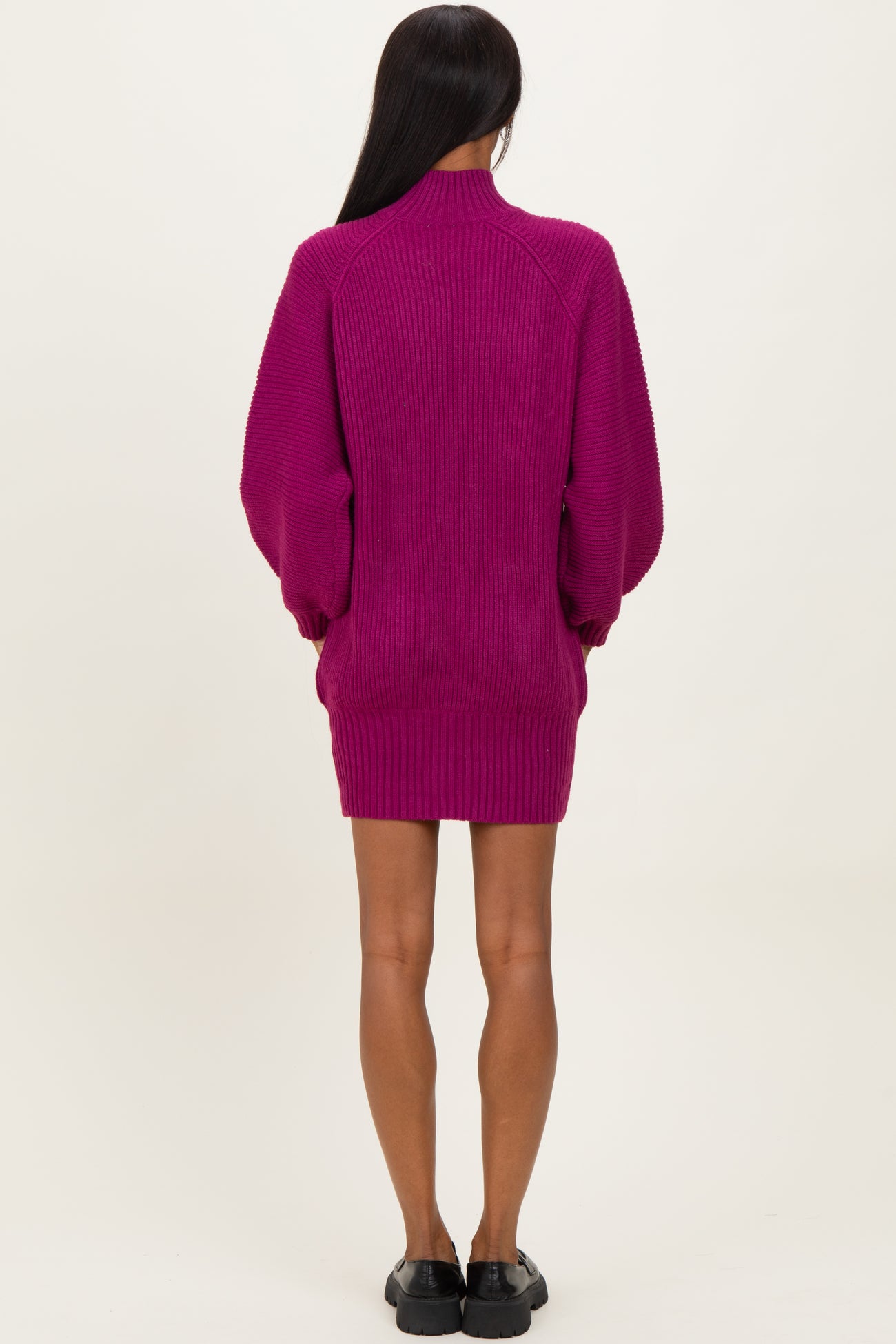 woman wearing a fuchsia oversized sweater dress with long sleeves and a high collar, viewed from the back