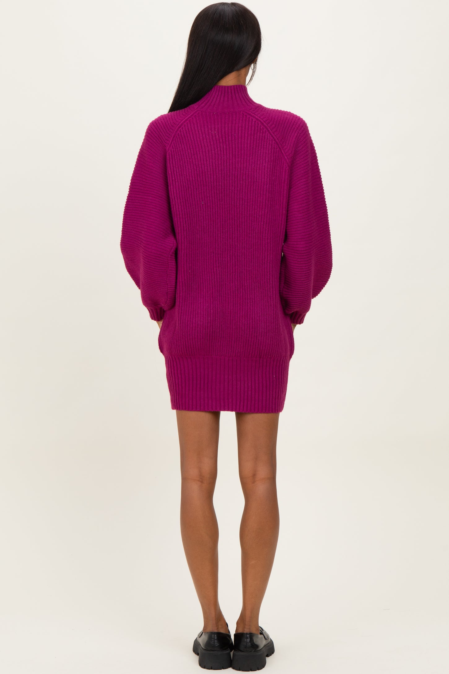 woman wearing a fuchsia oversized sweater dress with long sleeves and a high collar, viewed from the back